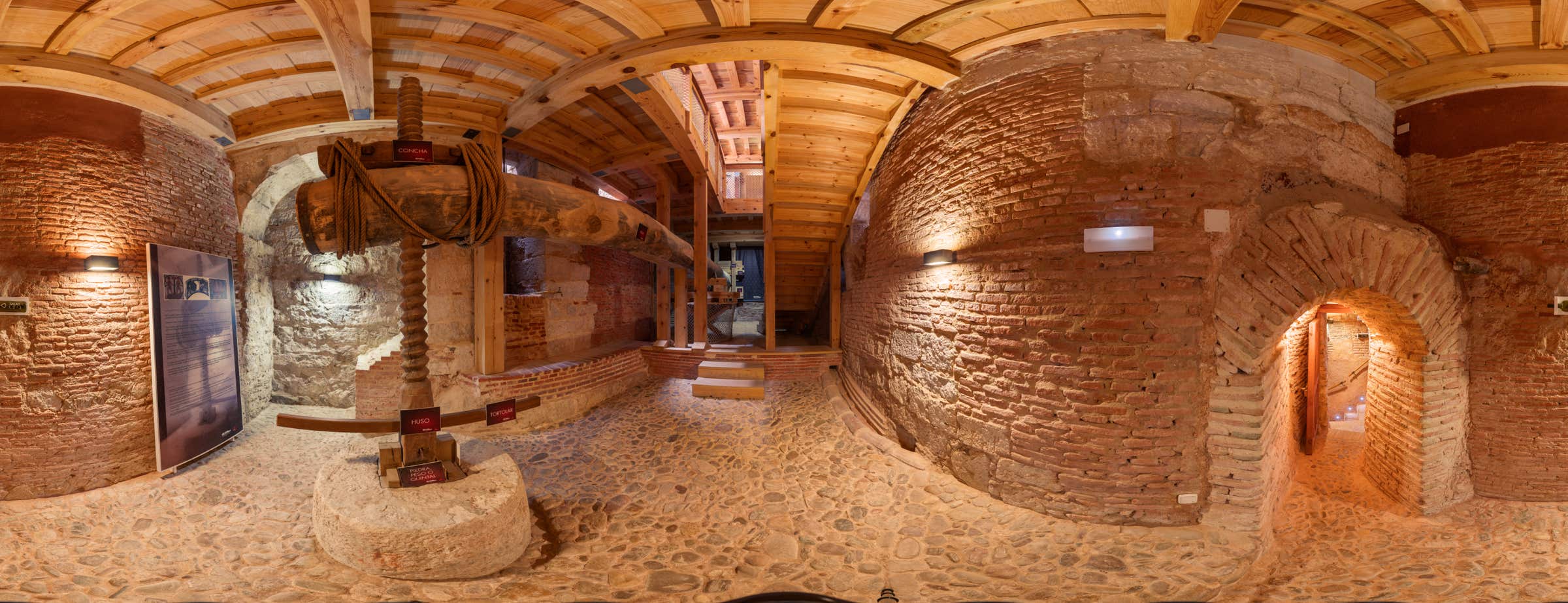 Imagen panorámica de 360° del interior del museo que muestra una gran prensa de madera utilizada para extraer el zumo de la uva.