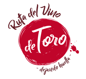 The Ruta del Vino de Toro logo is a red irregular circle, with other 2 smaller irregular circles on the right side, that are very similar to the drops that wine leaves when that is poured and accidentally stain a white surface. On top of the big red circle, a writing in brown appears mentioning "Ruta del Vino de", which is Spanish for "Wine Route of". Inside the circle, the previous words are completed by a white writing of "Toro". On the lower side of the big red circle, there are other 2 words "dejando huella", which is Spanish for leaving footprints.