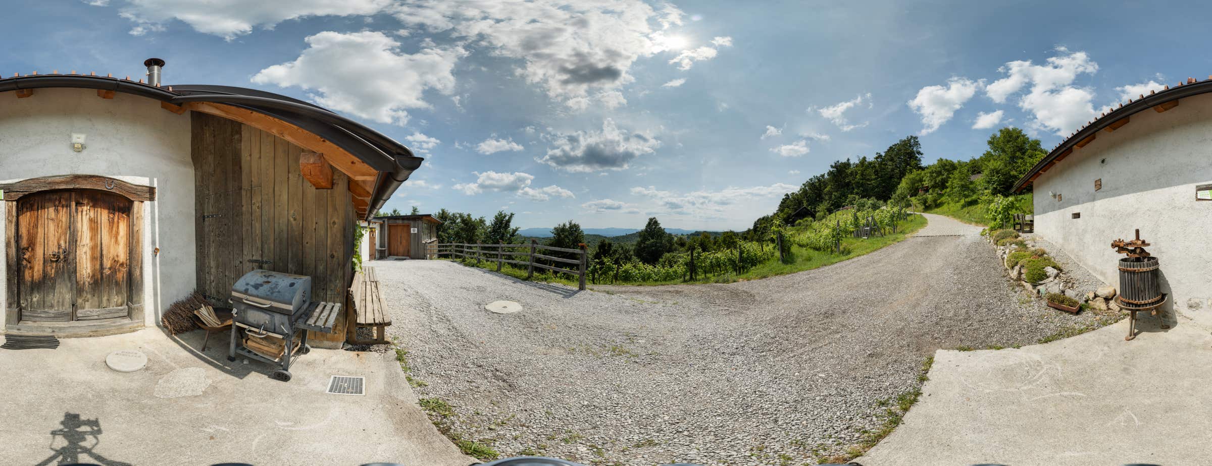 Panoramic image outside of a Škatlar showing its entrance area and the view over the vineyard right next to the building. 